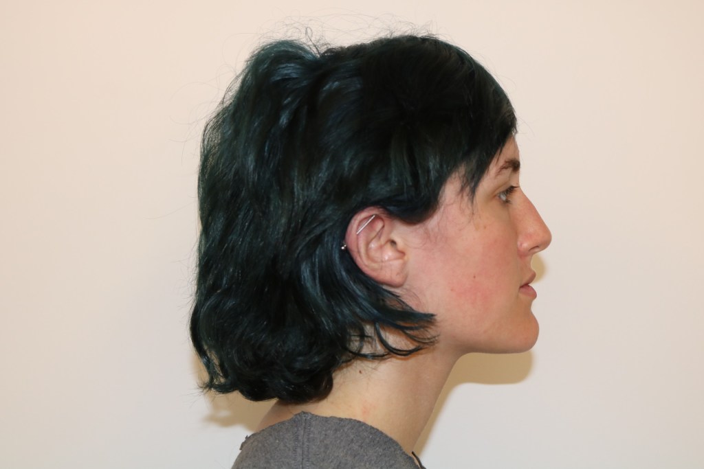 Profile view: person with short dark hair, neutral expression, light top