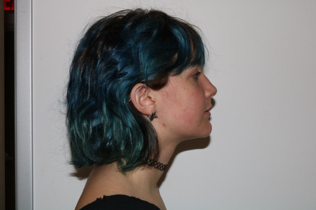 Profile view: person with blue hair, dark top, facing right